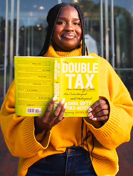 A woman smiles while holding a copy of "The Double Tax" book in her hands.